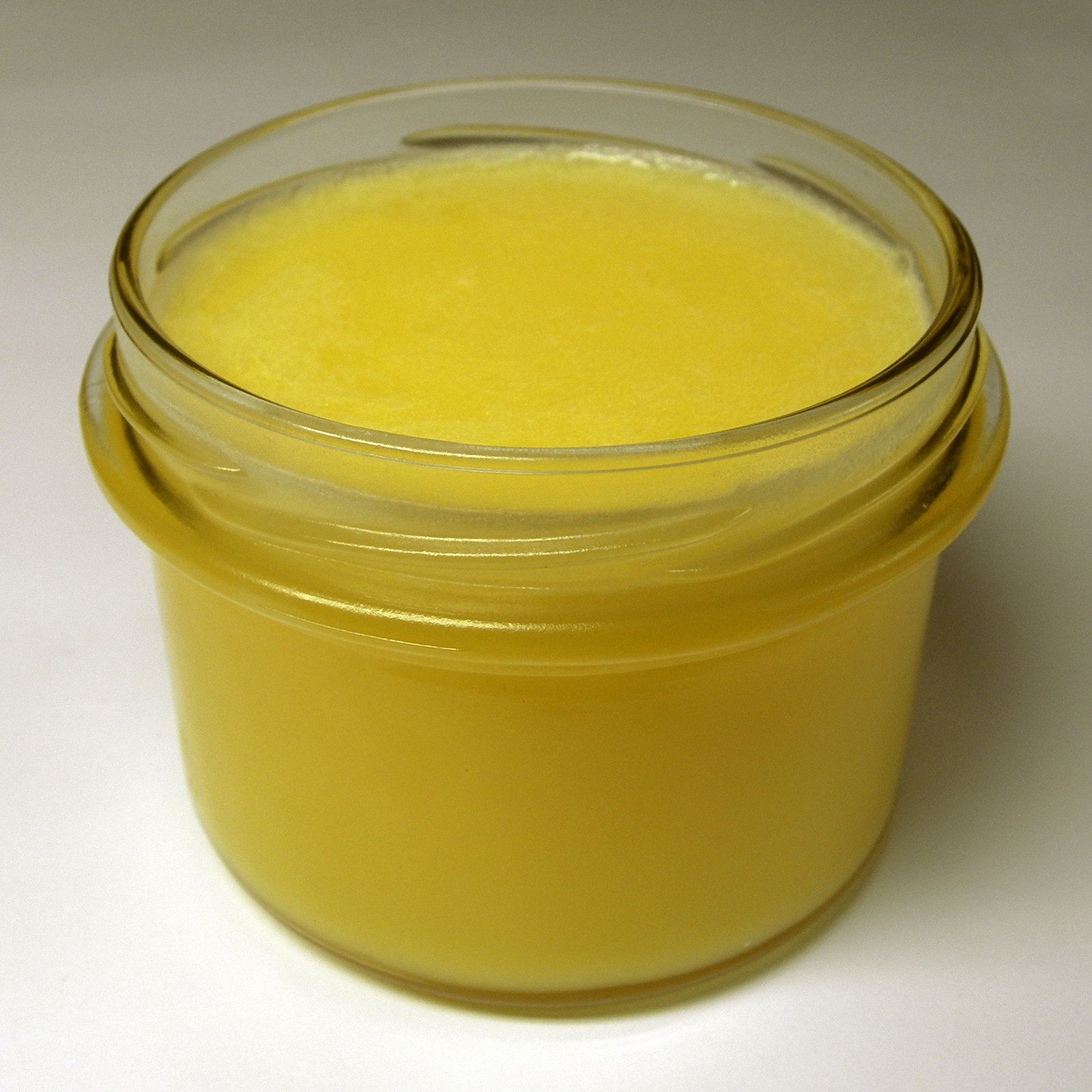 A glass jar of golden ghee against a clean white background