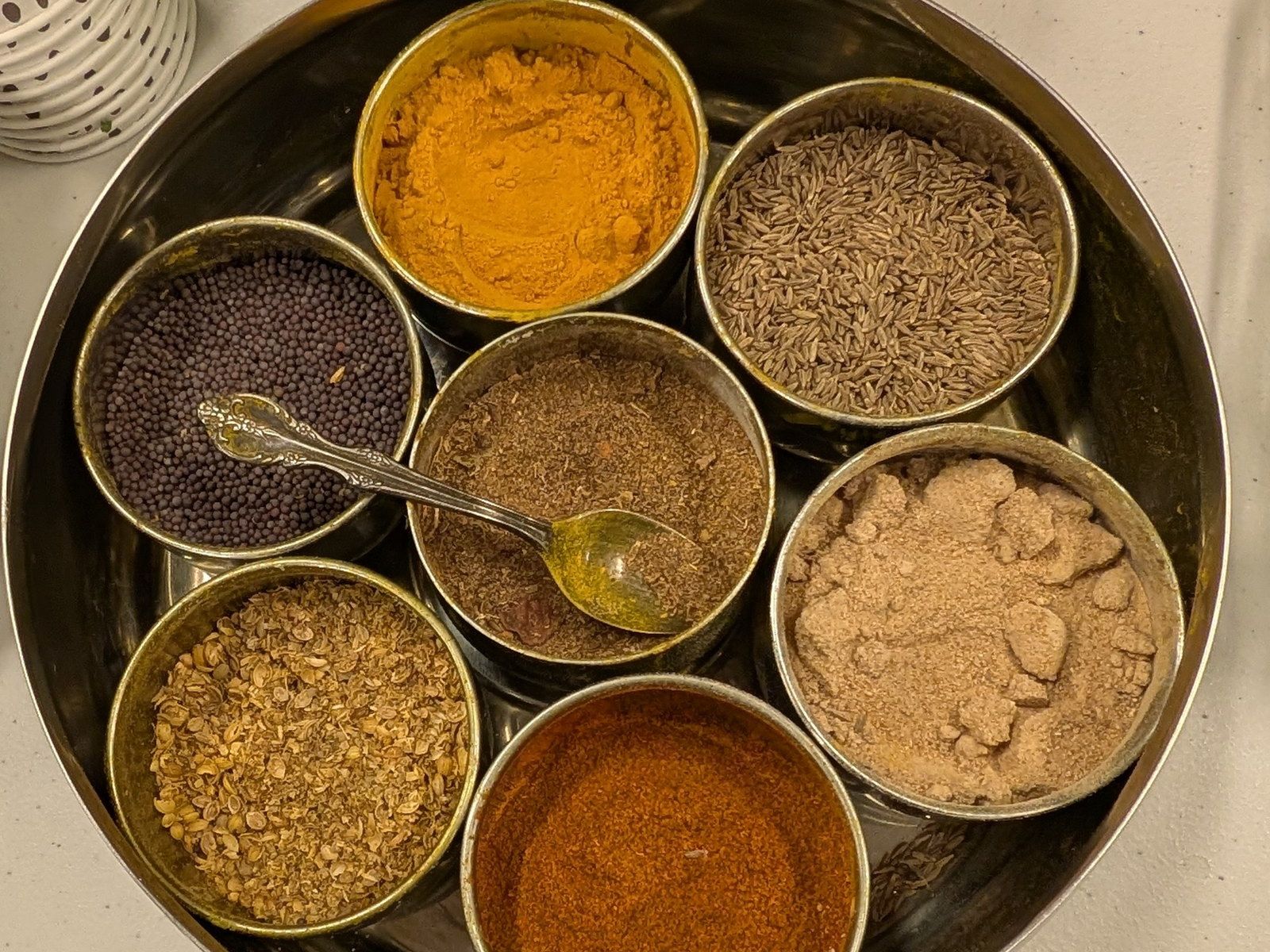 A stainless steel masala dabba filled with colourful Indian spices
