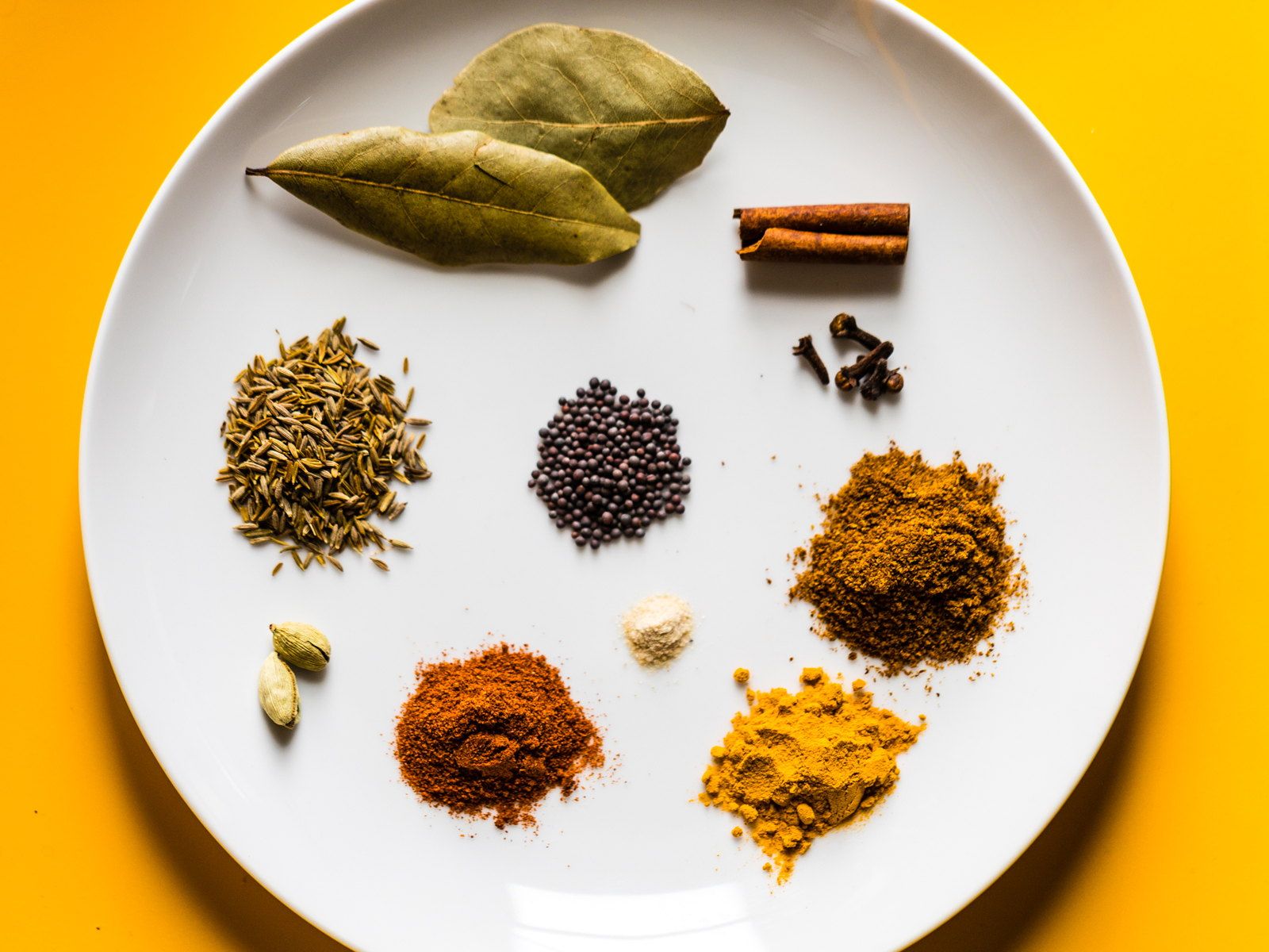 Whole Indian spices — bay leaf, cinnamon, cardamom and turmeric — on a plate